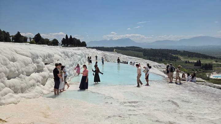 Crowds walk and wade in the turquoise thermal pools of Pamukkale's white travertine terraces.