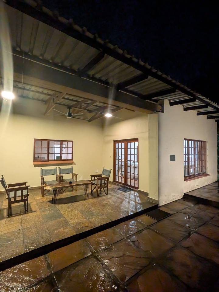 Simple covered patio with wooden chairs, a fan and tiled floor lit by warm ceiling lights.