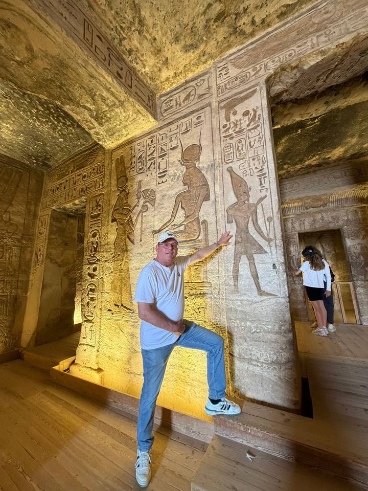 Visitor points to intricate hieroglyphs illuminated inside an ancient sandstone temple chamber.