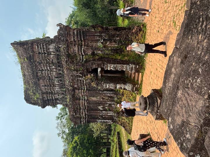 Visitors explore a red-brick Cham tower partially overgrown with vegetation at My Son Sanctuary.