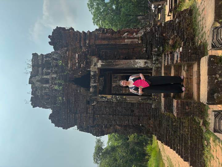 A traveler holding a pink fan stands on the steps of an ancient Cham ruin at My Son Sanctuary.