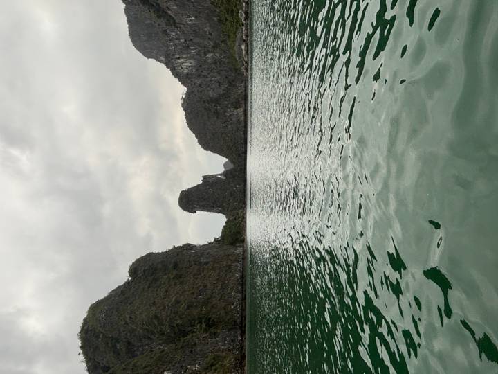 Emerald waters surrounded by limestone karst cliffs in cloudy Halong Bay.