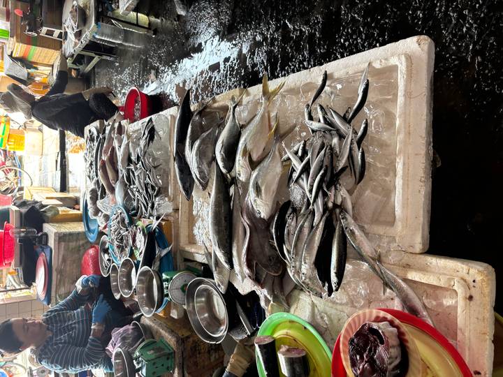 Market stall displays a variety of fresh fish on ice while vendors prepare seafood.