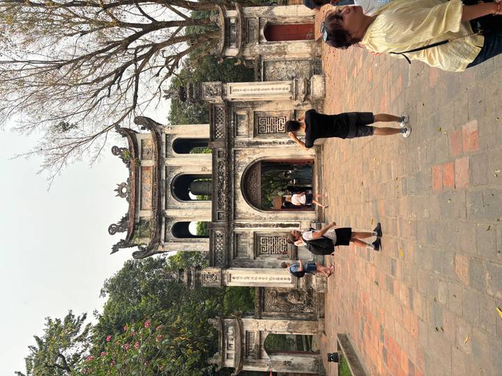 Travelers photograph the historic main gate of the Temple of Literature with leafless trees overhead.