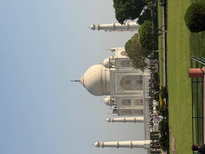 Side view of the Taj Mahal rising above green lawns under a clear blue sky