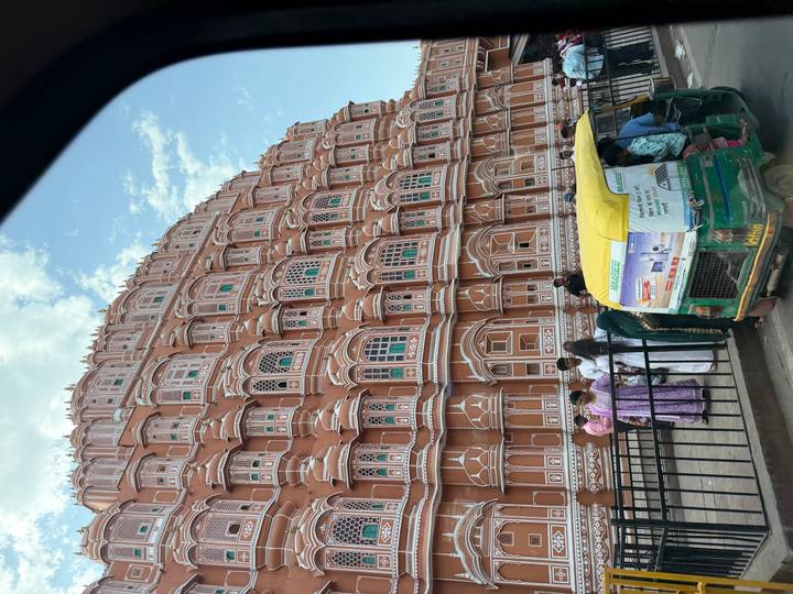 Hawa Mahal's ornate pink façade with tuk-tuk and pedestrians passing in Jaipur