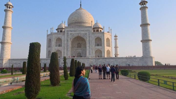 Tourists posing along the walkway in front of the Taj Mahal at sunrise.