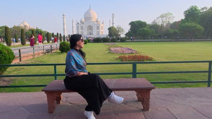 Woman seated on a bench with the Taj Mahal framed in the background.