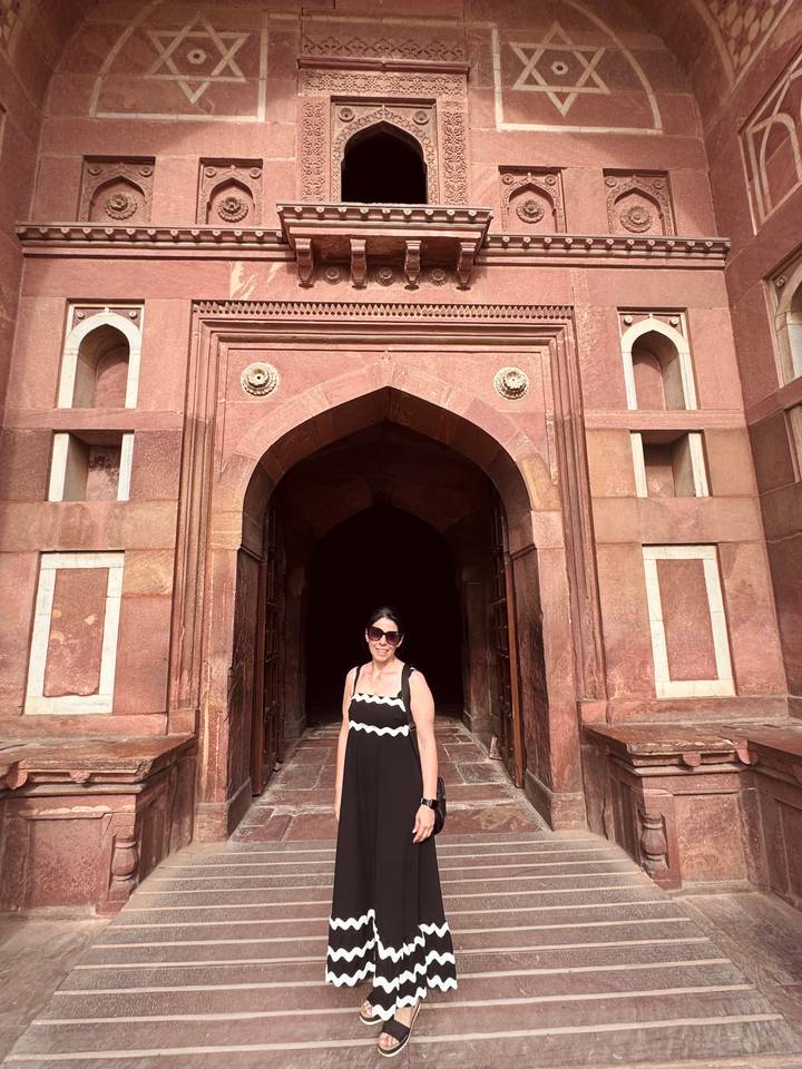 Woman standing before a red sandstone Mughal gateway with ornate arches.