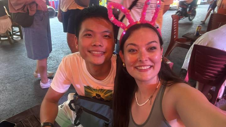 Selfie of two friends at a lively night market, one wearing glowing bunny ears.