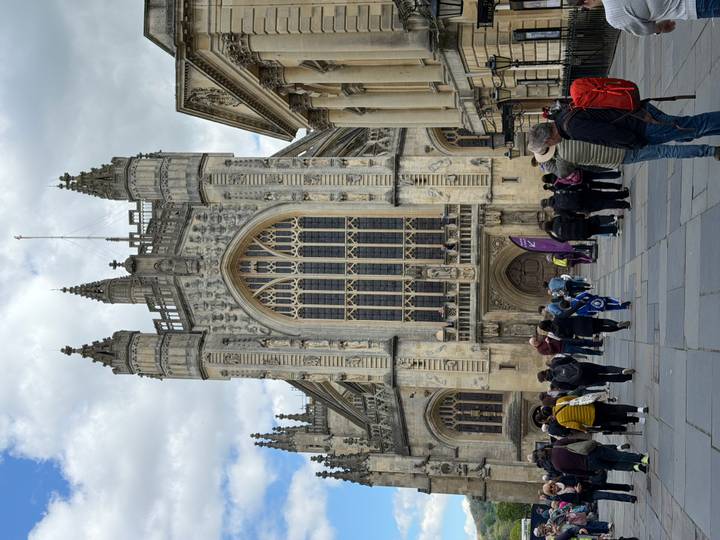 Visitors milling outside the ornate Gothic façade and huge window of Bath Abbey.
