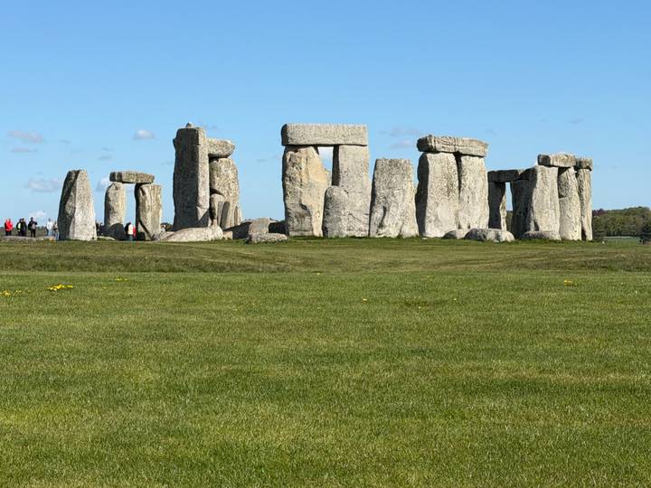 Iconic stone circles of Stonehenge standing on a bright green meadow under a clear blue sky.