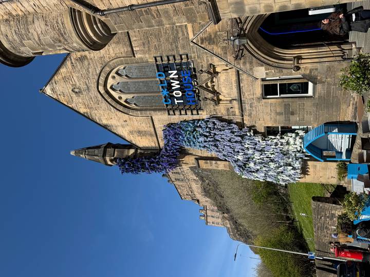 Stone building adorned with a vivid cascade of blue and white flowers, Edinburgh Castle on the hill behind.