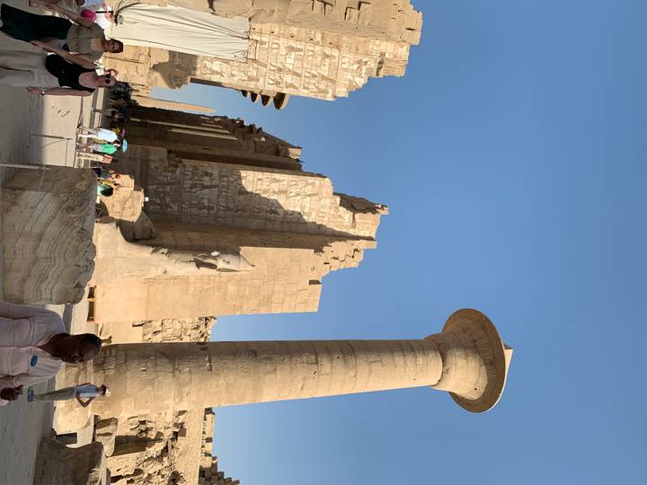 Massive column and ruined walls of Karnak Temple complex under clear blue sky.