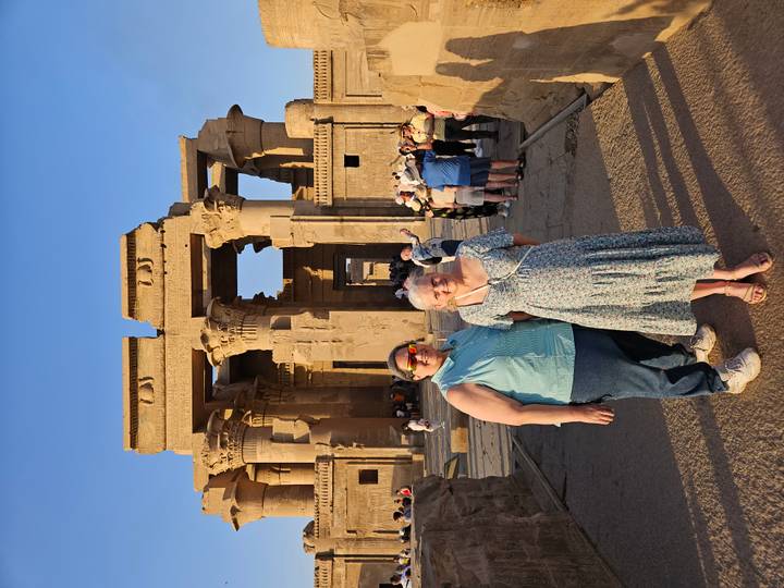 Two travellers posing in front of the stone columns of Kom Ombo Temple at golden hour