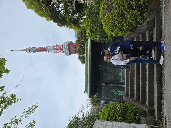 Couple embraces on stone steps with Tokyo Tower rising behind lush greenery.