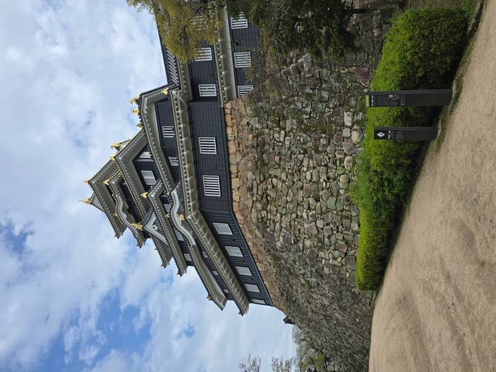 Black-walled Okayama Castle with gold roof ornaments towers above its massive stone base under blue skies.