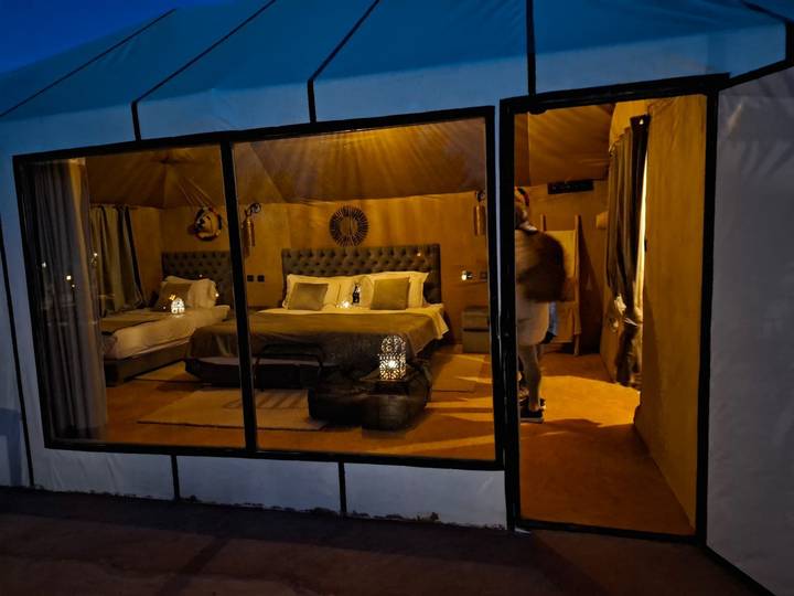 Chic desert glamping tent interior with twin beds, lanterns and warm golden lighting.