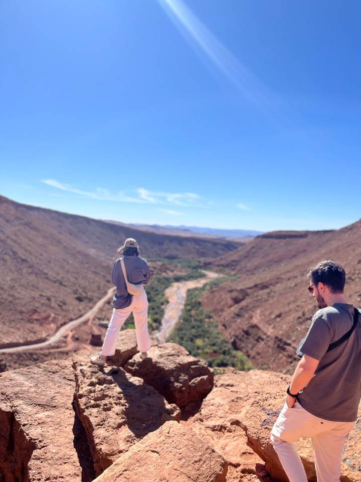 Travelers admire a winding river far below from a rocky canyon viewpoint under clear skies.