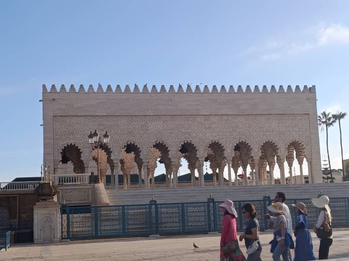 The Mausoleum of Mohammed V with its ornate arches and tourists passing in front.