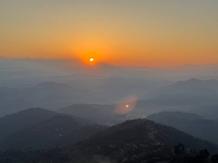 Soft orange sunrise over layered Himalayan foothills fading into mist.