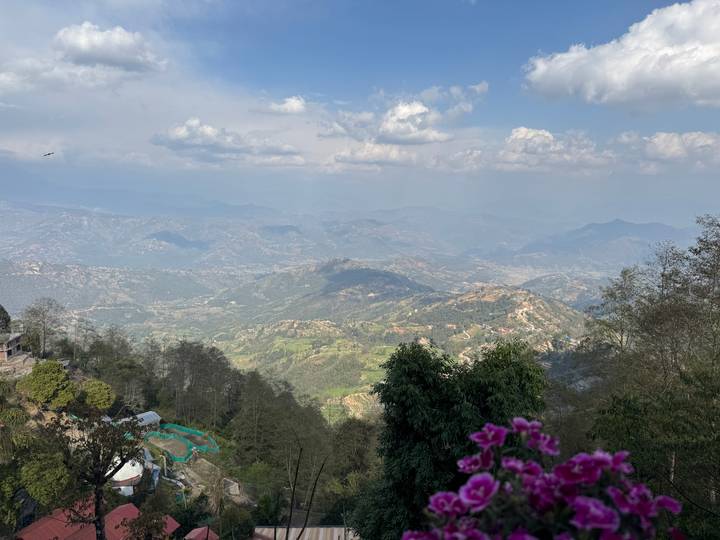 Expansive mountain valley view with patchwork farms beneath a partly cloudy sky.