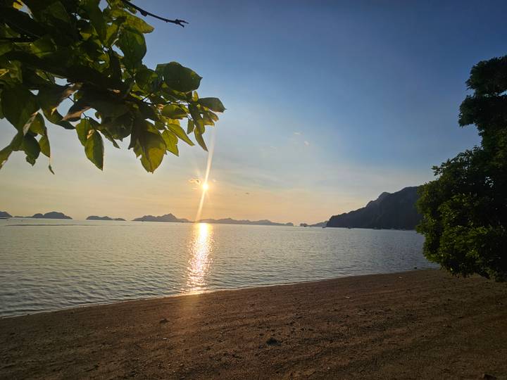 Golden sunset reflects as a bright streak over tranquil sea with silhouettes of islands on the horizon.