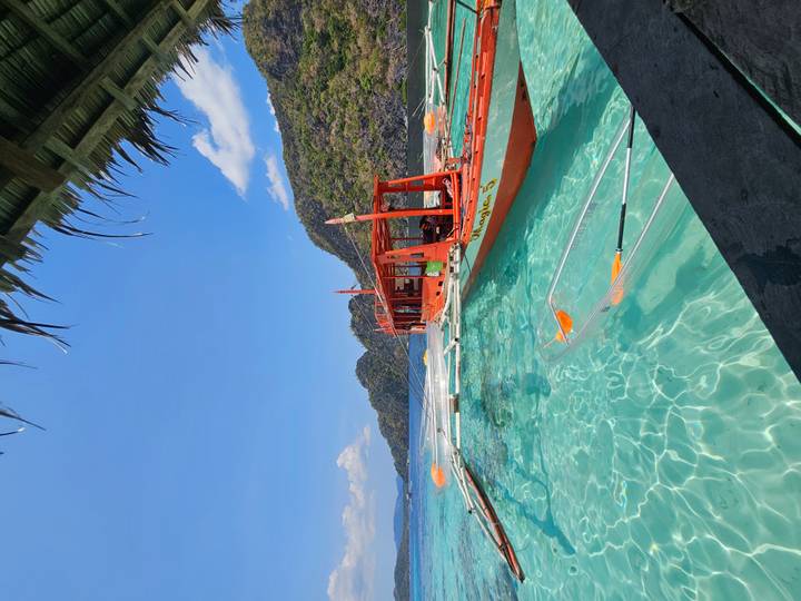 Traditional Filipino outrigger boat moored in crystal-clear turquoise waters with limestone cliffs in the background.