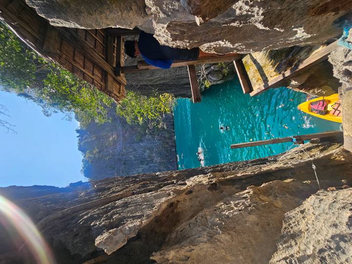 View through narrow limestone gorge to a vivid blue lagoon where swimmers enjoy the cool water and a yellow kayak awaits.