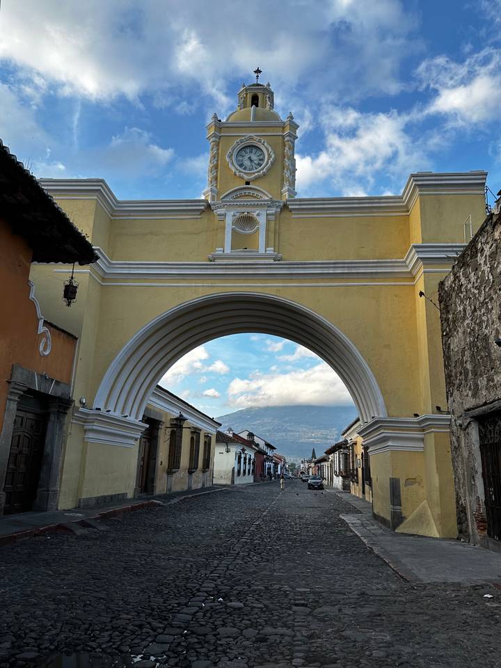 Iconic yellow Santa Catalina Arch frames a distant volcano above Antigua's colonial street.