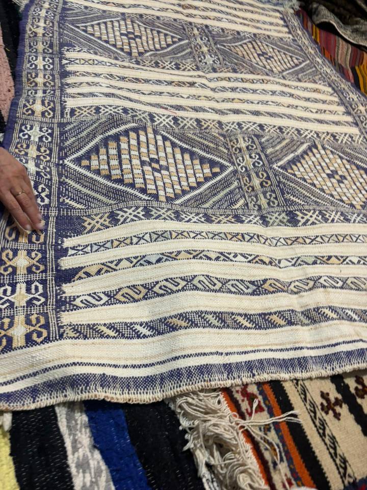 A craftsman’s hand rests on an intricately patterned Berber rug featuring blue and cream designs.
