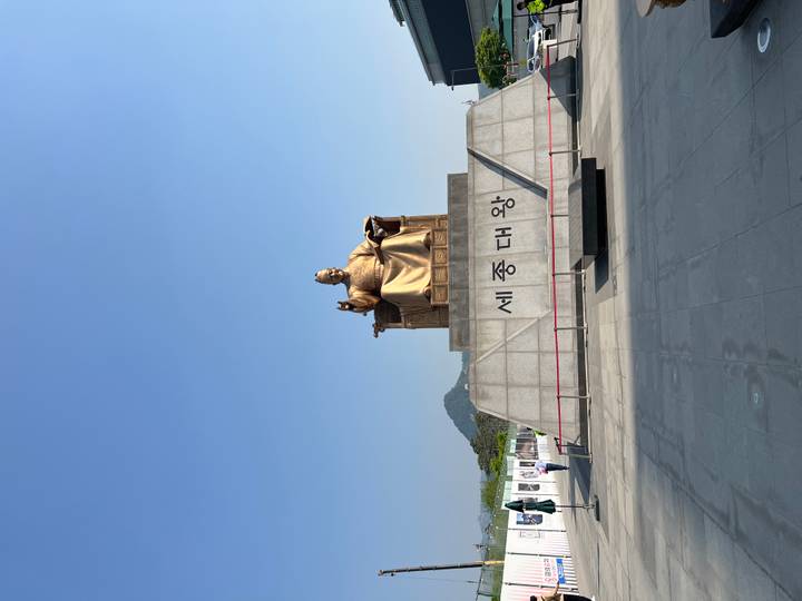 Golden seated statue of King Sejong on an expansive plaza under a clear blue sky.