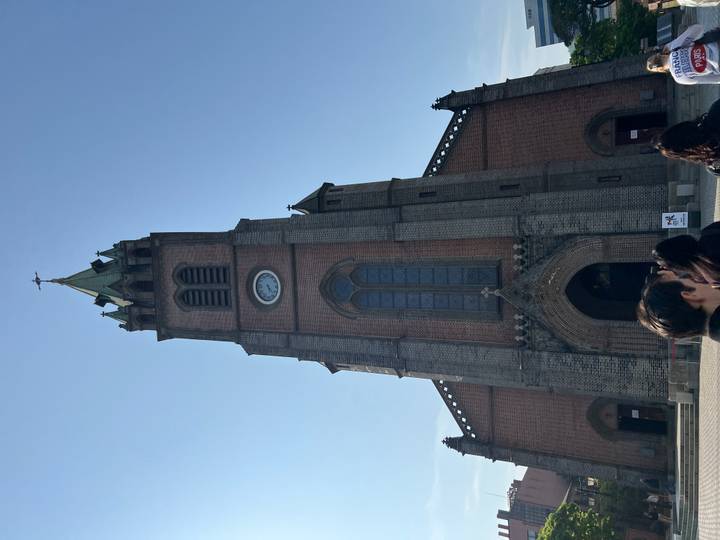 Gothic-style church tower rising into a clear sky with visitors gathered at its entrance.