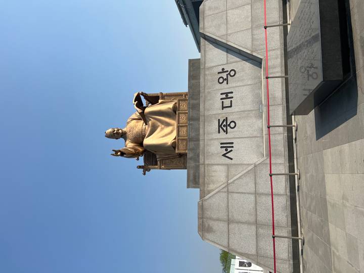 Close view of the golden King Sejong statue against a bright blue sky.