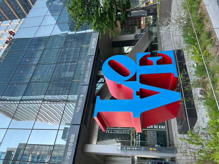 Large red and blue LOVE sculpture in front of modern glass buildings in Seoul.