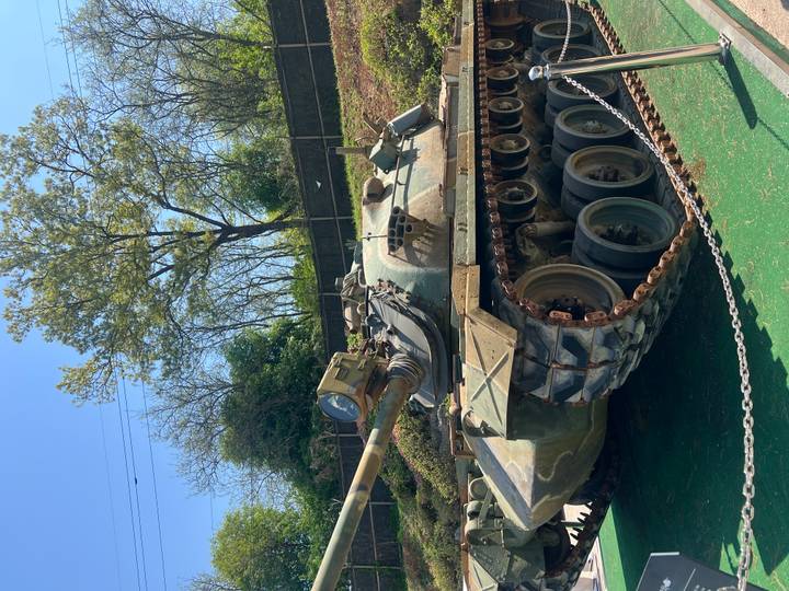 Close side view of a military tank displayed outdoors with trees in background.
