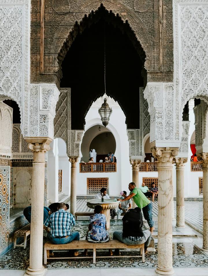 Interior of an ornate historic building with carved arches and columns, visitors observing the intricate details.
