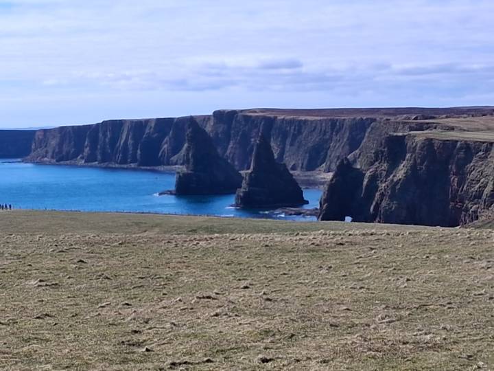 Dramatic sea stacks and sheer cliffs frame a vivid blue bay along Scotland’s rugged northern coast.