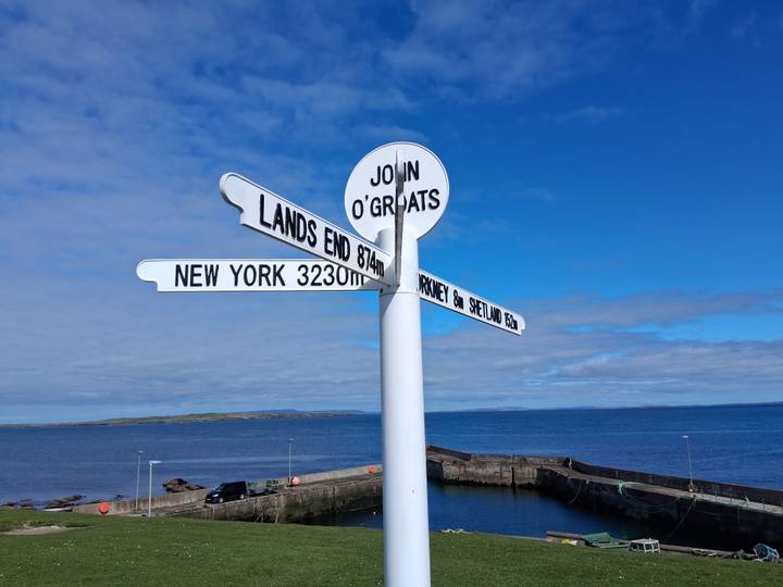 Iconic John O’Groats white signpost points to global destinations against a bright blue Scottish sky and sea.