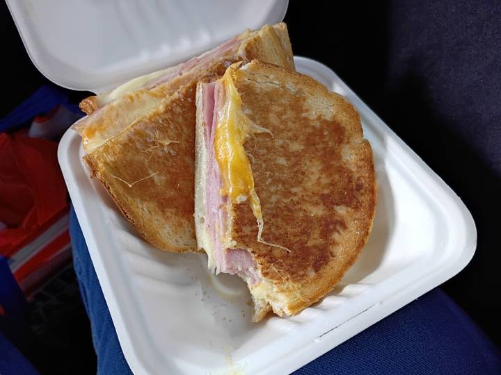 Close-up of toasted ham and cheese sandwich served in a disposable tray.