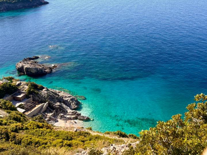 Turquoise Adriatic cove with clear water, rocky outcrops and small hidden beach viewed from above.
