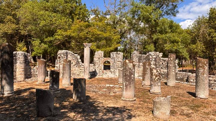 Ruined stone temple with standing circular columns in a wooded archaeological site.