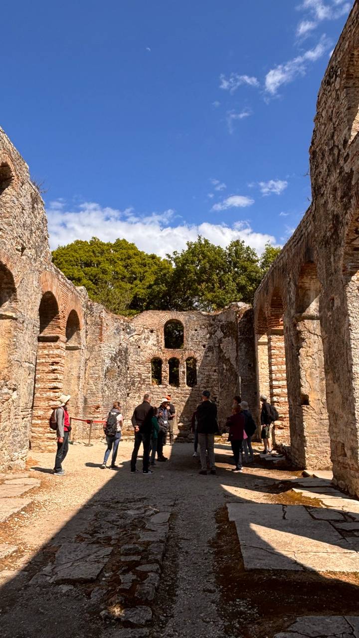 Tour group explores the interior of ancient stone basilica ruins with arched windows.