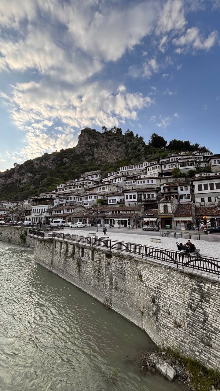 Tiered white Ottoman houses climbing a steep hillside above a riverfront promenade in evening light.