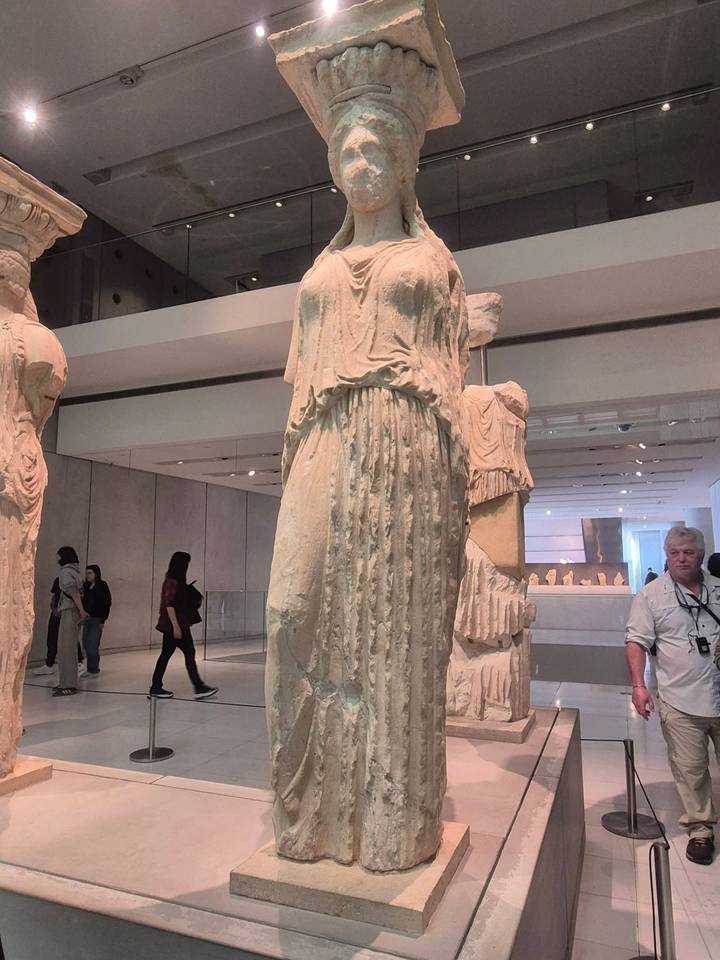 Marble Kore statue displayed inside a modern museum hall with visitors observing ancient artifacts.