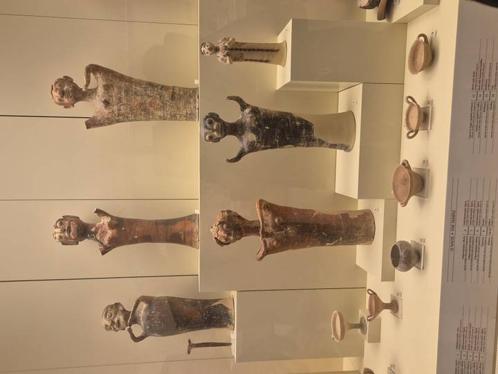 Display of small terracotta figurines and pottery vessels arranged on museum shelves with descriptive labels.
