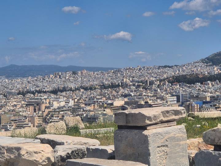Panoramic view of Athens' densely packed buildings sprawling across hills beneath a blue sky.
