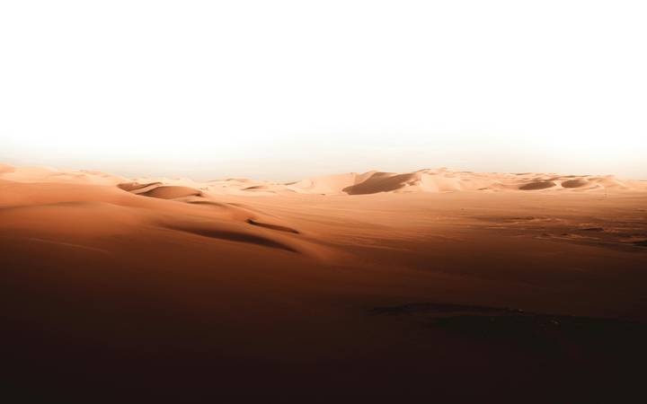 Vast sun-lit sand dunes form smooth curves beneath a bright, hazy sky.