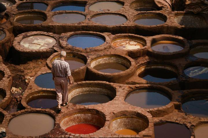 A worker stands among round stone vats of dye in an ancient tannery filled with colorful liquids.