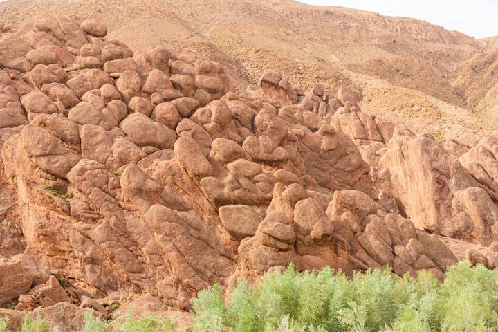 Clustered reddish rock pillars known as the Monkey Fingers rise above green shrubs at the gorge base.